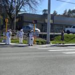 Group of protesters in white clothing holding signs at a street corner with a fast-food restaurant in the background (McDonald's).