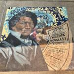 Colorful sidewalk mural featuring a close-up portrait of Frederick Douglass with a lecture poster and a crowd in the background.