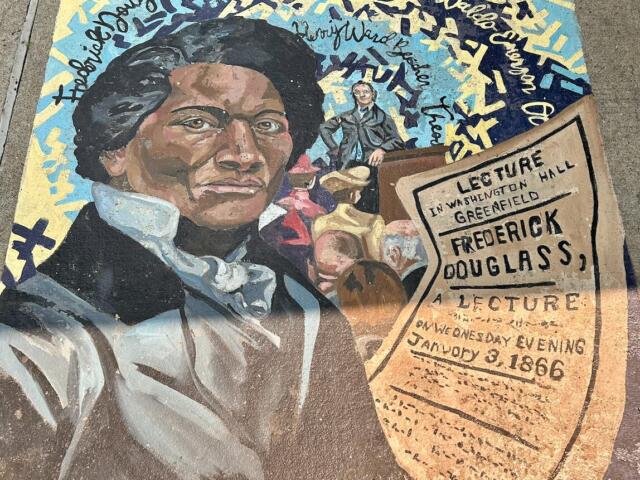 Colorful sidewalk mural featuring a close-up portrait of Frederick Douglass with a lecture poster and a crowd in the background.