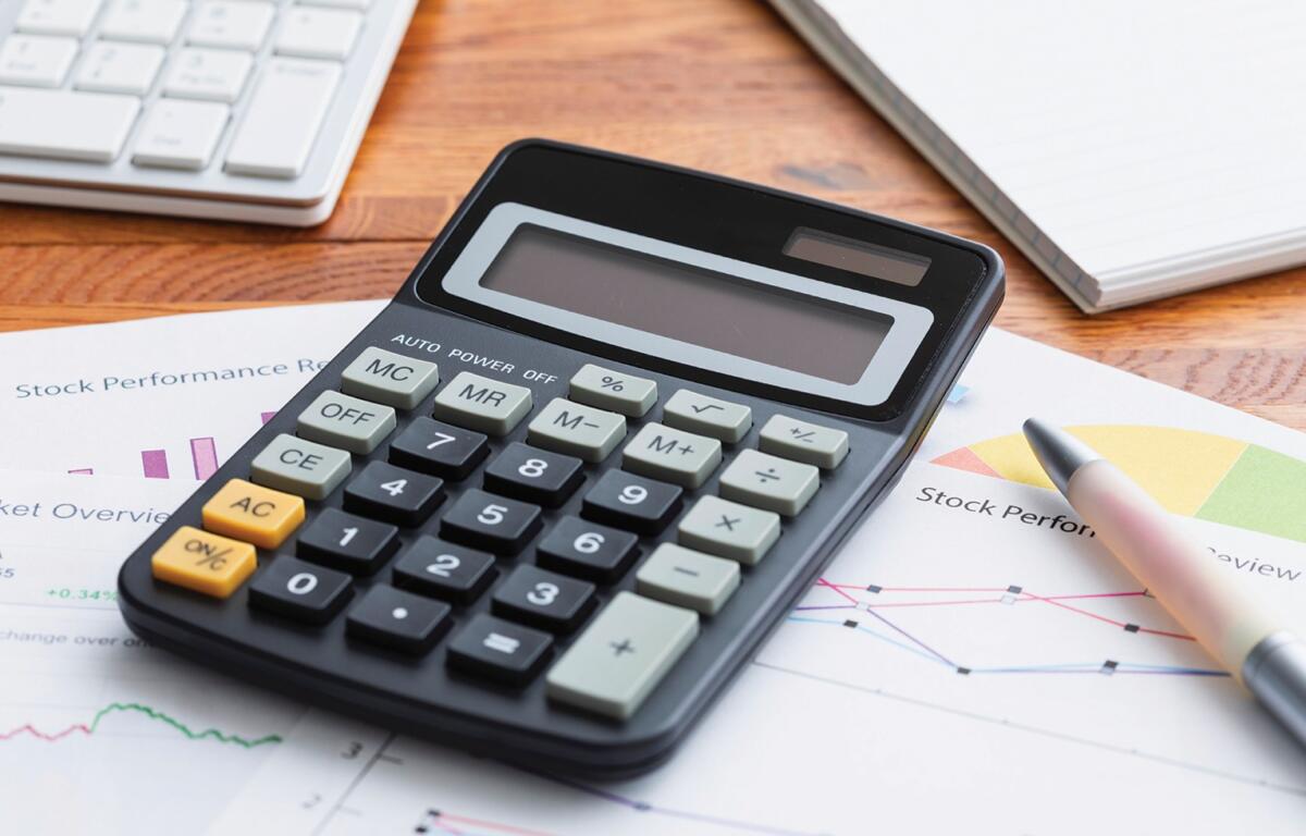 Calculator resting on stock performance reports with a pen and charts nearby on a wooden desk