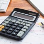 Calculator resting on stock performance reports with a pen and charts nearby on a wooden desk
