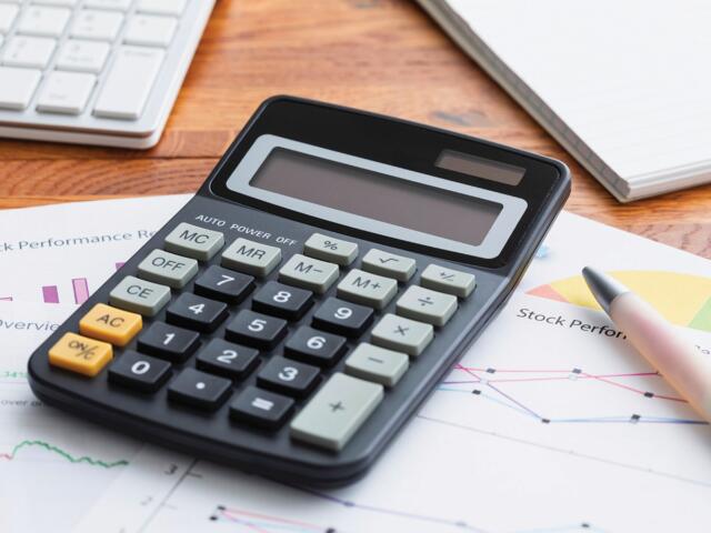 Calculator resting on stock performance reports with a pen and charts nearby on a wooden desk