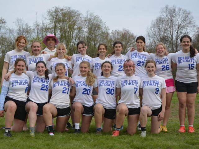 Group of players in white 'Four Rivers Ultimate' shirts posing together on a grassy field outdoors, smiling at the camera.