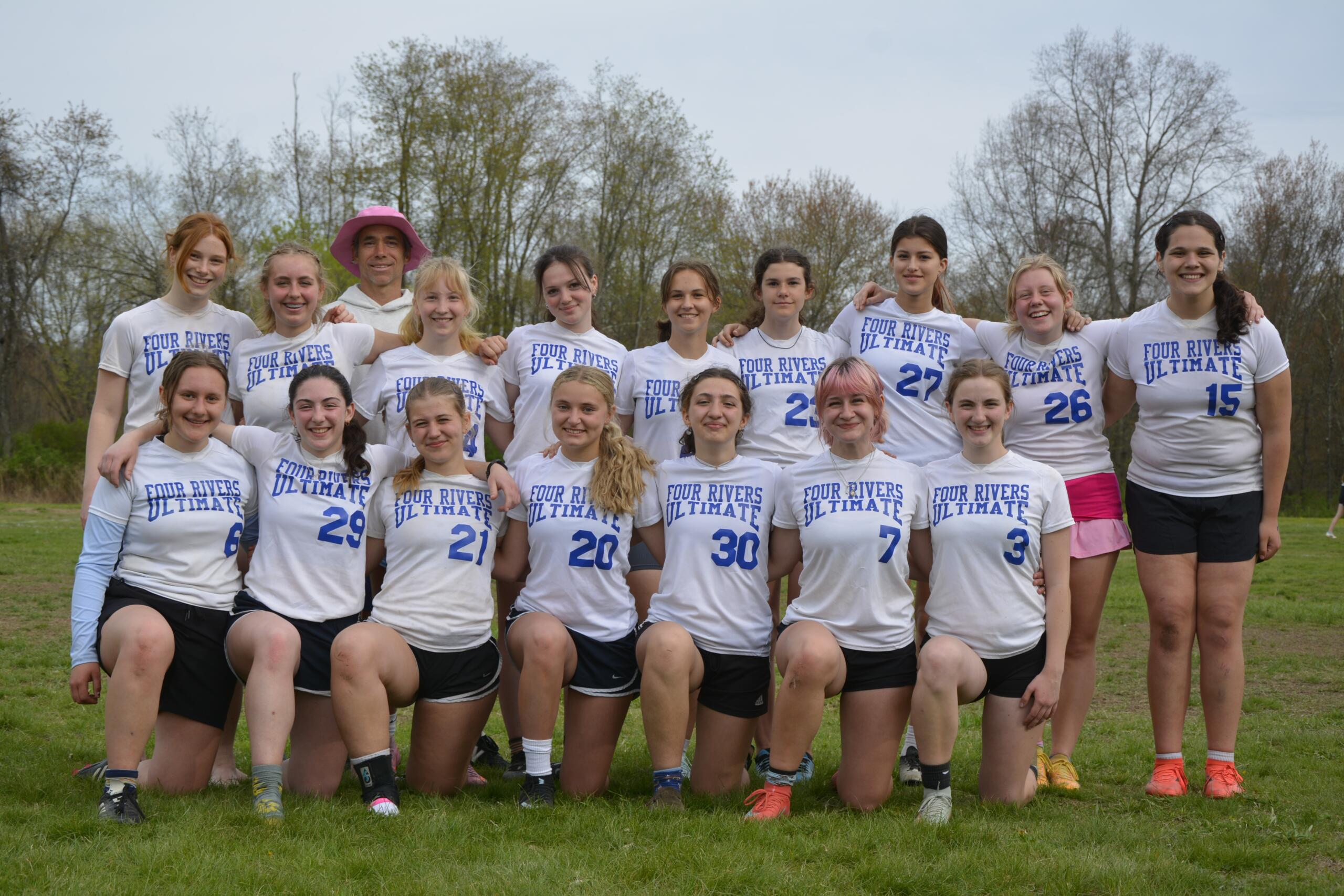 Group of players in white 'Four Rivers Ultimate' shirts posing together on a grassy field outdoors, smiling at the camera.