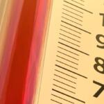 Close-up of a thermometer with red liquid against a yellow panel, showing scale marks and numbers 70–100.