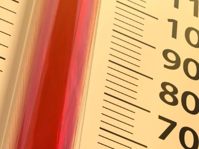 Close-up of a thermometer with red liquid against a yellow panel, showing scale marks and numbers 70–100.