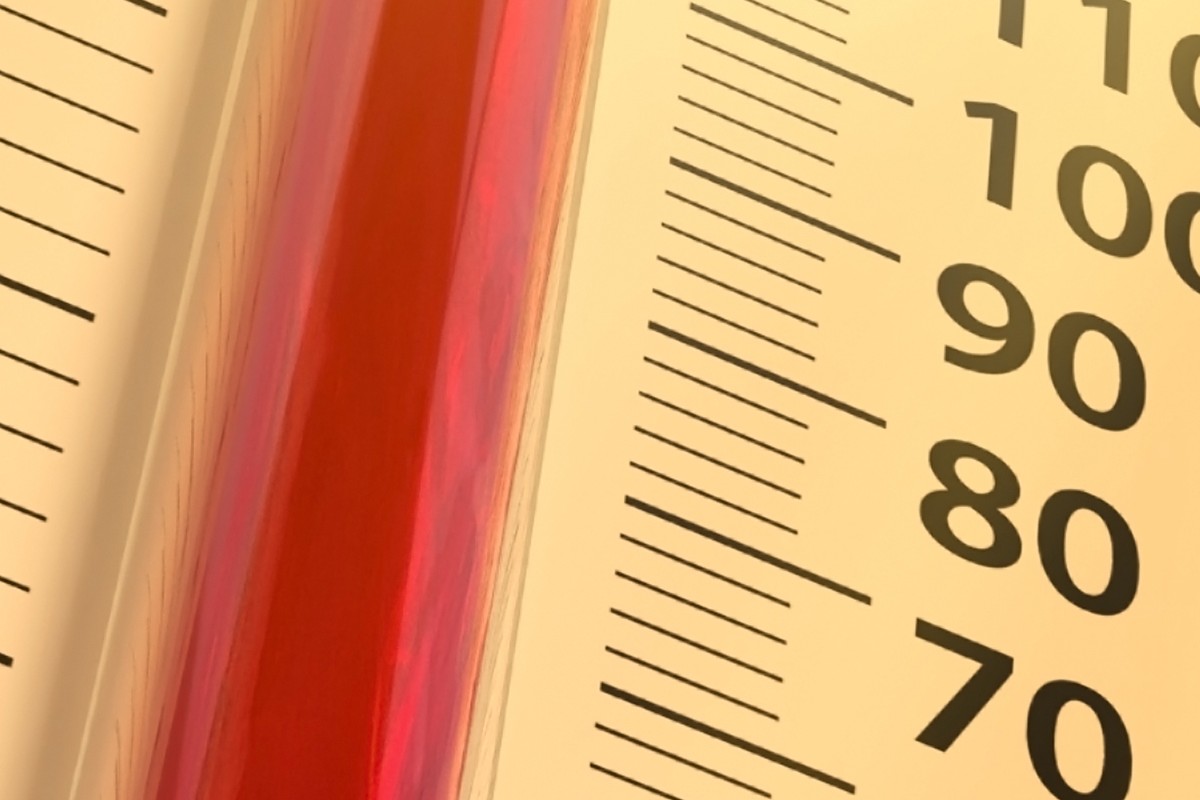 Close-up of a thermometer with red liquid against a yellow panel, showing scale marks and numbers 70–100.