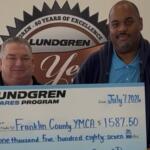Two men hold a large Lundgren Cares Program check for $1,587.50 to Franklin County YMCA, dated July 7, 2026.
