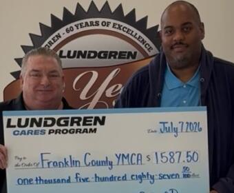 Two men hold a large Lundgren Cares Program check for $1,587.50 to Franklin County YMCA, dated July 7, 2026.