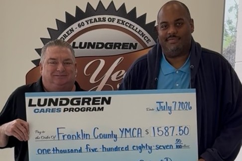 Two men hold a large Lundgren Cares Program check for $1,587.50 to Franklin County YMCA, dated July 7, 2026.
