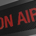 Red 'ON AIR' text behind a dark perforated metal grille, signaling live broadcasting.