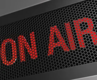 Red 'ON AIR' text behind a dark perforated metal grille, signaling live broadcasting.