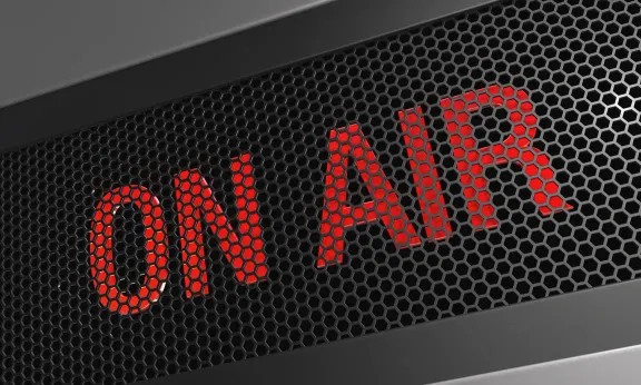 Red 'ON AIR' text behind a dark perforated metal grille, signaling live broadcasting.